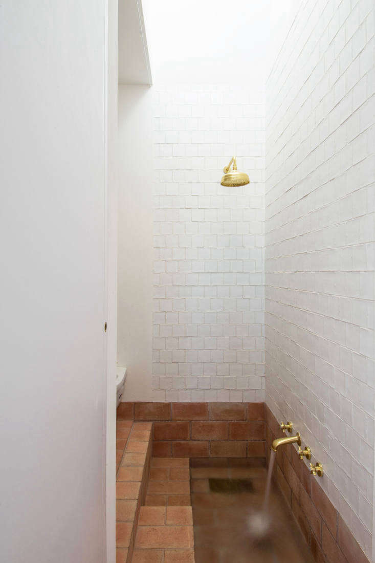 the shower is clad in handmade matte white porcelain tiles. the brass shower fi 31